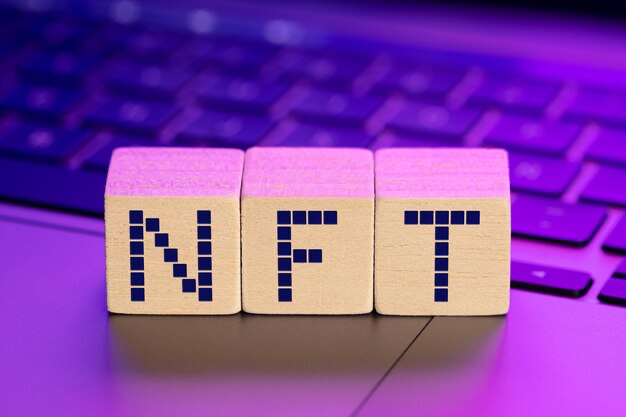 The word nft on wooden blocks on a laptop with colorful lights