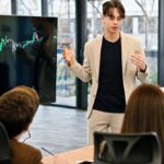 A young man presenting financial data on a screen to a group