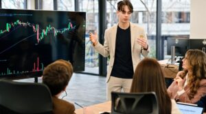 A young man presenting financial data on a screen to a group